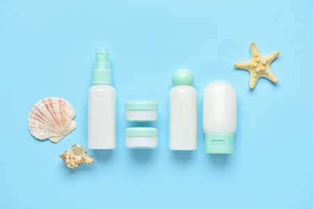 Travel bottles, jars with cosmetic products and sea shells on blue background