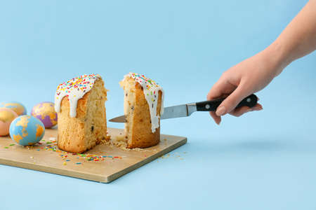 Woman cutting delicious Easter cake on blue background