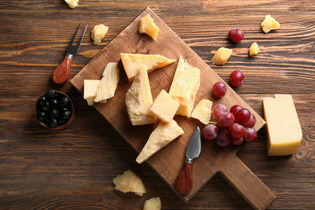 Board with pieces of tasty Parmesan cheese on wooden backgroundの写真素材