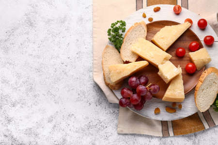 Wooden board with pieces of tasty Parmesan cheese and bread on light backgroundの写真素材