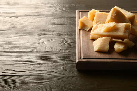 Board with pieces of tasty Parmesan cheese on brown wooden background, closeupの写真素材