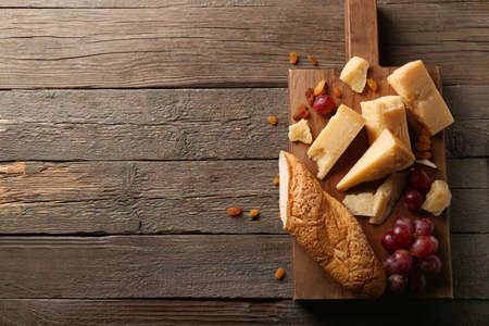 Board with pieces of tasty Parmesan cheese, grape and bread on wooden background