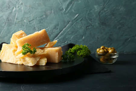 Wooden board with pieces of tasty Parmesan cheese on table, closeup
