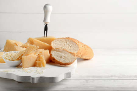 Board with pieces of tasty Parmesan cheese and bread on white wooden background