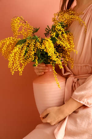 Woman holding vase with mimosa flowers on color backgroundの写真素材
