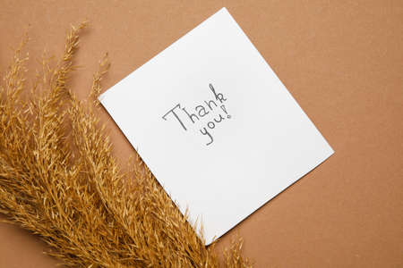 Paper sheet with text THANK YOU and dry reeds on brown background
