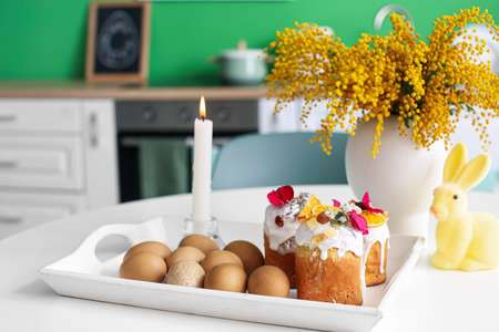 Tray with Easter cakes, eggs, burning candle and mimosa flowers on dining tableの写真素材