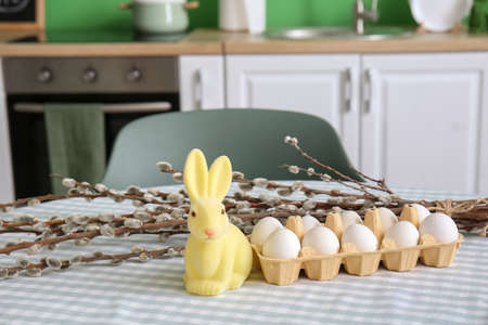 Holder with Easter eggs, rabbit and pussy willow branches on dining table