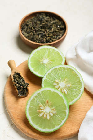 Wooden board with slices of ripe bergamot fruits and dried tea leaves on light background, closeup