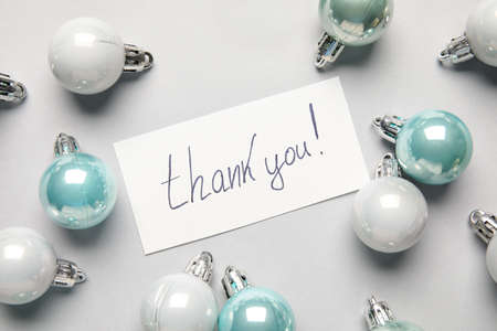 Paper sheet with text THANK YOU and Christmas balls on light background