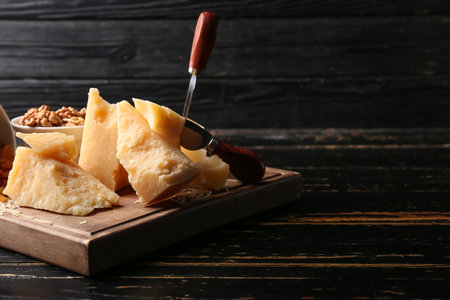 Board with pieces of tasty Parmesan cheese on black wooden background, closeupの写真素材