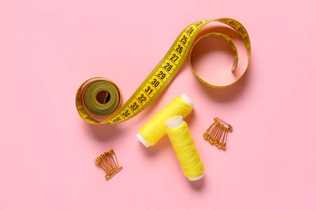 Thread spools, measuring tape and safety pins on pink backgroundの写真素材