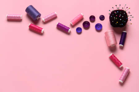 Thread spools, ball pins and buttons on pink background