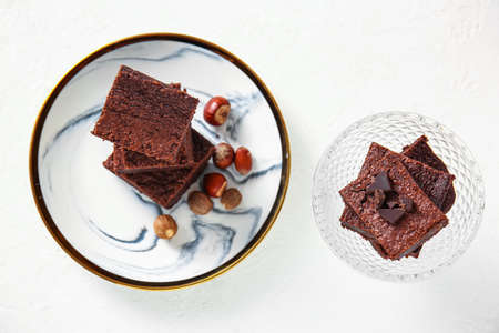 Plate and bowl with pieces of tasty chocolate brownie on light background