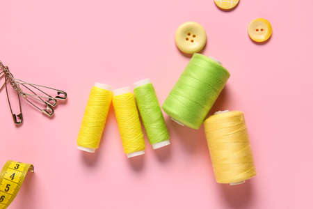 Thread spools, safety pins and buttons on pink background