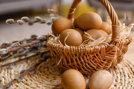 Basket with Easter eggs and pussy willow branches on table, closeup