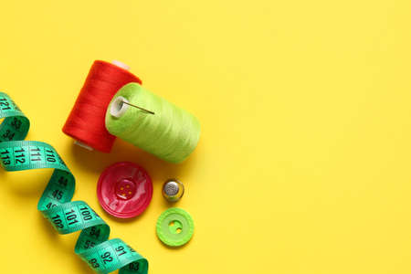 Thread spools, measuring tape and buttons on yellow backgroundの写真素材