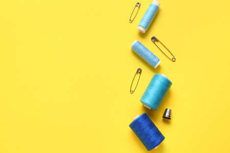 Thread spools and pins on yellow background