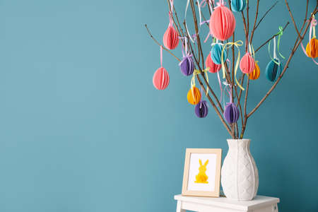 Photo frame and vase with tree branches decorated for Easter celebration on stepladder stool near...