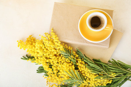 Beautiful mimosa branches, cup of coffee and books on light backgroundの写真素材