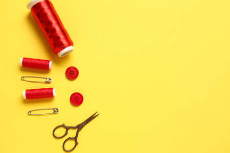 Thread spools, scissors, buttons and pins on yellow backgroundの写真素材