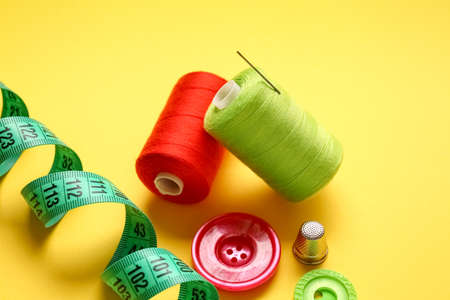 Thread spools, measuring tape and buttons on yellow backgroundの写真素材