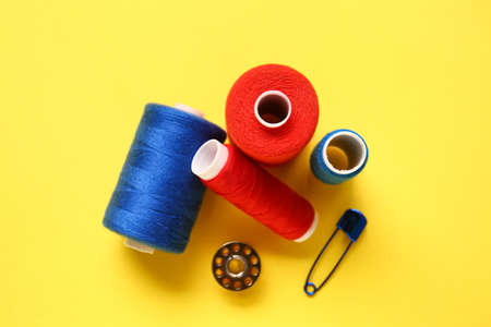 Thread spools and safety pin on yellow background