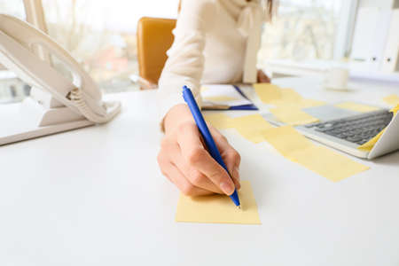 Young manager writing on sticky note paper at her workplaceの写真素材