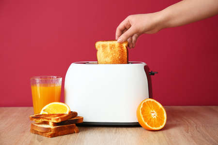 Woman taking bread slice from toaster and glass of juice on wooden tableの写真素材