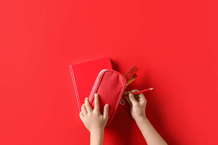 Child's hands with pencil case and book on red background