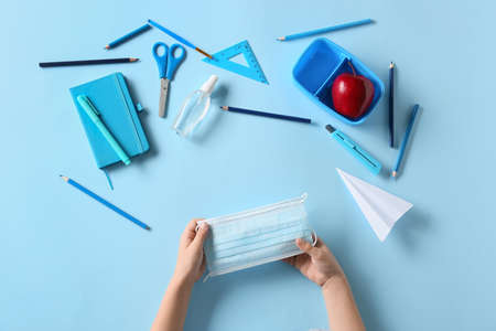 Child's hands with medical mask, stationery, bottle of sanitizer and apple on color backgroundの写真素材