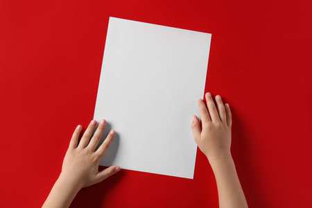 Child's hands with blank sheet of paper on red backgroundの写真素材