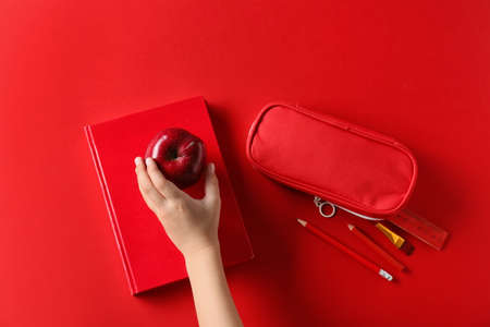 Child's hand with apple, book and pencil case on red backgroundの写真素材