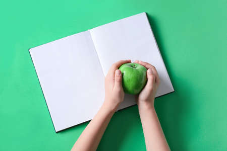 Child's hands with apple and blank book on green backgroundの写真素材