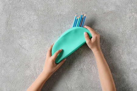 Child holding pencil case with color pencils on light background