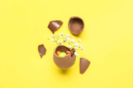 Delicious chocolate egg with filling and flowers on yellow background