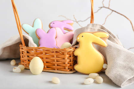 Wicker basket with tasty Easter cookies in shape on bunny and candies on light backgroundの写真素材
