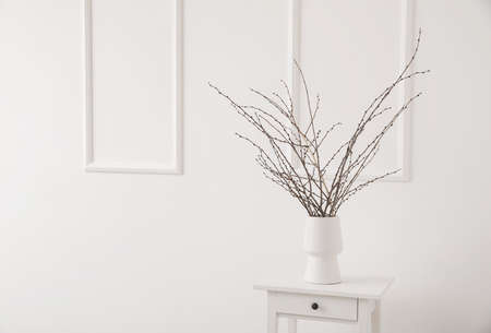 Vase with tree branches on white table near light wallの写真素材