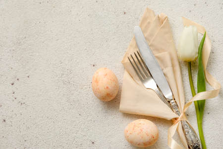 Stylish table setting for Easter celebration with tulip flower on light background