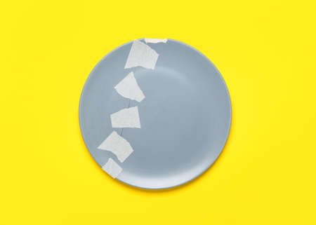 Broken ceramic plate with adhesive tape on yellow backgroundの写真素材