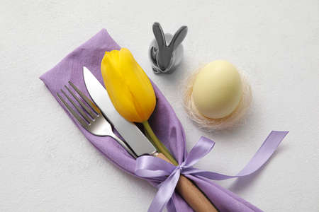 Stylish table setting for Easter celebration with tulip flower on light background