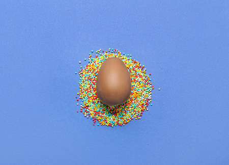 Delicious chocolate egg and sprinkles on blue background