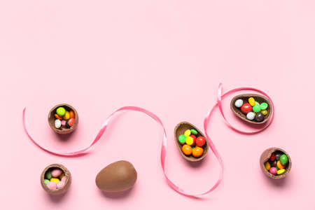 Delicious chocolate eggs with candies fillings on pink background