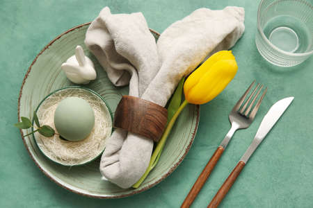 Stylish table setting for Easter celebration with tulip flower on green background