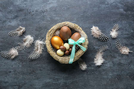 Composition with Easter eggs in nest and feathers on dark background