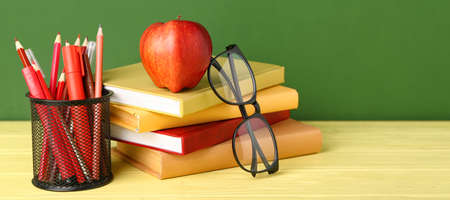 School stationery, books, apple and eyeglasses on table against green backgroundの写真素材