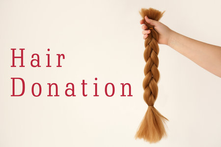 Female hand with braided hair strand on light background. concept of donationの写真素材