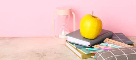 School stationery with apple and hourglass on table against pink backgroundの写真素材