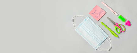 Set of school stationery and medical mask on light background with space for text
