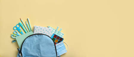 Backpack with school stationery and medical mask on beige background with space for textの写真素材